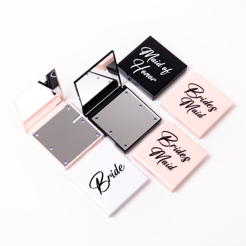 May include: Four compact mirrors with LED lights. The mirrors are white, black, and pink. The mirrors have the words "Bride", "Maid of Honor", and "Bridesmaid" written on them.