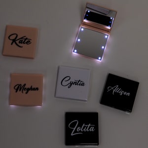 May include: Five small, square, compact mirrors with LED lights. Each mirror has a different name on the front: Kate, Meghan, Cynthia, Allison, and Lolita. The mirrors are in various colors: pink, white, and black.