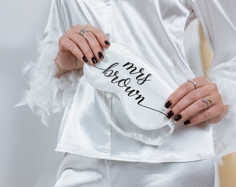 May include: White satin sleep mask with the text "mrs brown" in black lettering. The sleep mask is held by a person wearing a white satin robe with the name "inna" embroidered on the front.