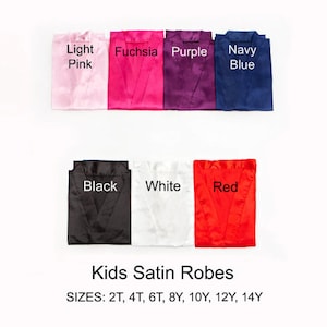 May include: A collection of folded satin robes in various colors: light pink, fuchsia, purple, navy blue, black, white, and red. The text "Kids Satin Robes" is displayed below the robes, along with size options.