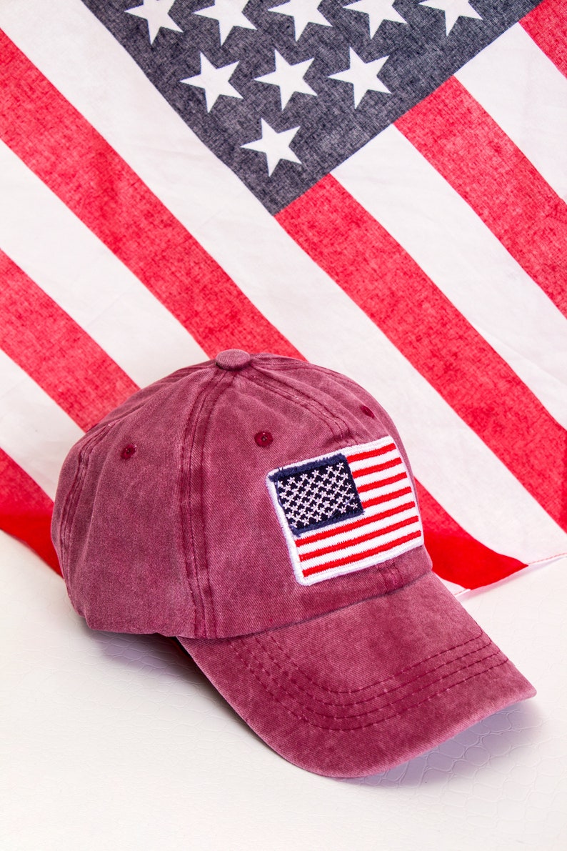 May include: A burgundy baseball cap with a small American flag patch on the front. The cap is made of a soft, distressed cotton fabric.
