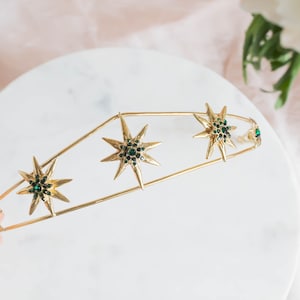 May include: Gold headband with a row of five green jeweled starbursts.