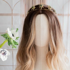 May include: A gold crown with green star accents. The crown is on a mannequin head with long, wavy, light brown hair.