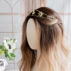 May include: Gold star crown with green gemstones, worn on a mannequin with long brown and blonde hair.