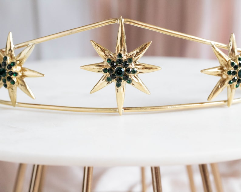 May include: Gold crown with three star-shaped embellishments, each with green rhinestones.
