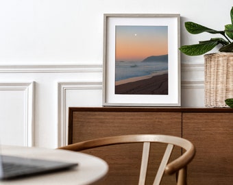 May include: A framed photograph of a beach scene with a sunset sky, ocean waves, and a sandy shore. The photo is hanging on a wall above a wooden cabinet.