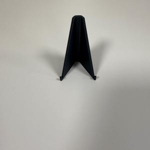 Peut inclure: Un support de présentation noir mat doté d'un profil en V avec deux petits crochets incurvés vers le haut à la base. Le support présente une colonne vertébrale centrale verticale et deux panneaux latéraux inclinés pour maintenir des objets.