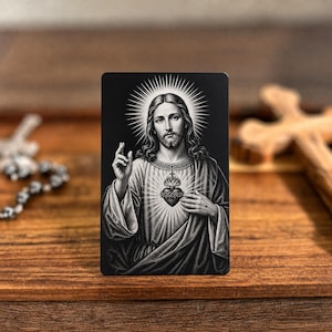 May include: A rectangular black and white metal card featuring a detailed illustration of the Sacred Heart of Jesus. The image depicts Jesus with a halo, a raised hand in blessing, and a heart encircled by thorns, rendered in high-contrast monochrome.
