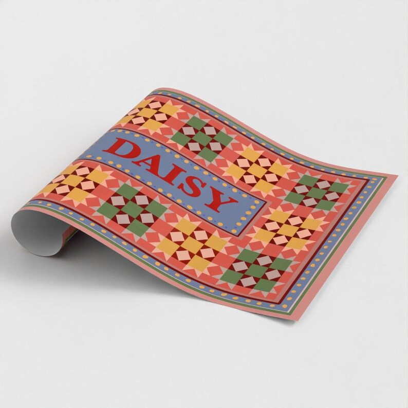 May include: A roll of wrapping paper featuring a repeating quilt-like pattern of yellow, green, and red geometric shapes on a coral background. A central blue horizontal band displays the word DAISY in bold red capital letters.