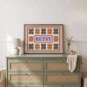 May include: A framed rectangular wall art piece featuring a quilt-inspired pattern of green, yellow, and white geometric star shapes surrounding a central rectangular panel with the name BETSY printed in large blue capital letters.
