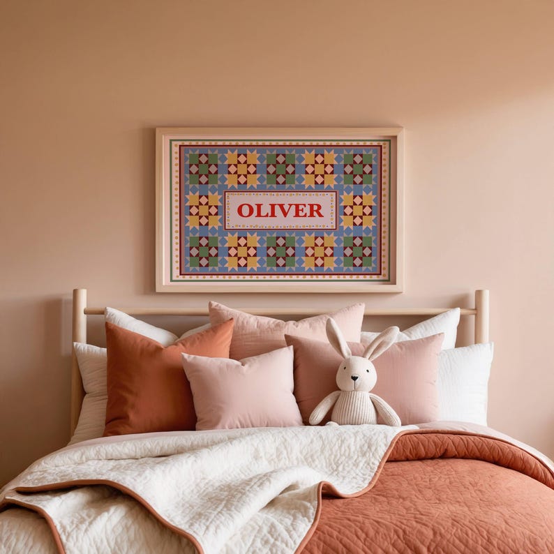 May include: A rectangular framed wall art print featuring a repeating geometric quilt-like pattern in shades of blue, green, yellow, and red. The center of the print contains a white rectangular panel with the name OLIVER printed in red letters.