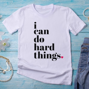May include: White t-shirt with black text that reads "I can do hard things" with a small pink heart.