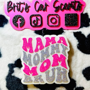 May include: Two car air fresheners. The top one is pink with the text "Brite's Car Scents" and social media icons. The bottom one is white with the text "Mama Mommy Mom Muh" in pink and silver glitter.