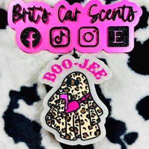 K&ouml;nnte beinhalten: Ein dekorativer Auto-Lufterfrischer in Form eines Geistes mit Leopardenmuster, der eine pinke Umh&auml;ngetasche tr&auml;gt und einen pinken Becher h&auml;lt. Dar&uuml;ber befindet sich ein pinkes Schild mit der Aufschrift Brit's Car Scents und Social-Media-Symbolen.