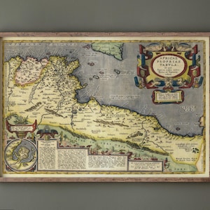 Puede incluir: Mapa antiguo enmarcado de África, con cartografía detallada, texto e ilustraciones. El mapa está en un marco de madera y se muestra contra una pared gris. Los colores del mapa incluyen tonos de azul, amarillo, verde y marrón.