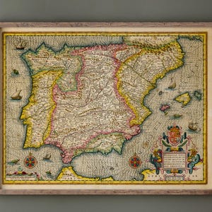 May include: Framed antique map of the Iberian Peninsula, featuring detailed cartography with yellow, pink, and green accents. The map includes nautical elements and decorative cartouches, set within a wooden frame.