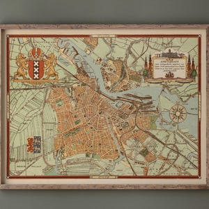 Può includere: Mappa vintage incorniciata di Amsterdam, Paesi Bassi, nei toni del marrone, verde e blu. La mappa presenta strade cittadine dettagliate, canali e aree circostanti, con elementi decorativi tra cui una rosa dei venti e uno stemma. La mappa è in una cornice di legno marrone chiaro.