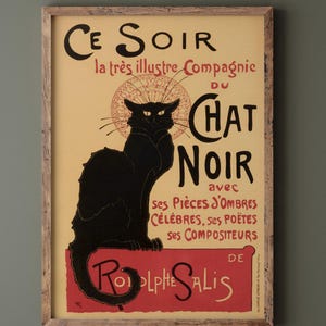 May include: A framed vintage poster featuring a black cat silhouette with the text "Ce Soir du Chat Noir" in black and red. The poster has a light yellow background and a wooden frame, showcasing a classic art nouveau design.