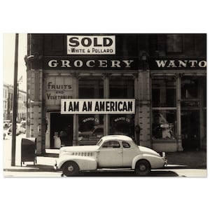 Può includere: Una fotografia in bianco e nero di un negozio di alimentari con un cartello che recita "SOLD by WHITE & POLLARD GROCERY WANTO". Un'auto è parcheggiata davanti al negozio con uno striscione che recita "I AM AN AMERICAN" appeso sopra.