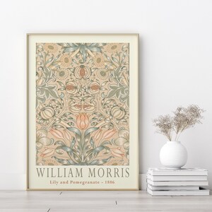 K&ouml;nnte beinhalten: Ein gerahmter Druck eines Vintage-Blumendesigns von William Morris, mit einem sich wiederholenden Muster aus Lilien und Granat&auml;pfeln in Gr&uuml;n-, Rosa- und Cremet&ouml;nen. Der Druck tr&auml;gt den Titel "Lily and Pomegranate - 1886".