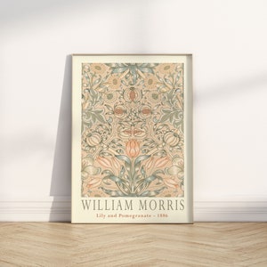 K&ouml;nnte beinhalten: Ein gerahmter Druck eines Vintage-Blumendesigns von William Morris mit dem Titel "Lily and Pomegranate - 1886". Das Design zeigt ein sich wiederholendes Muster aus Lilien, Granat&auml;pfeln und Bl&auml;ttern in Gr&uuml;n-, Rosa- und Cremet&ouml;nen.