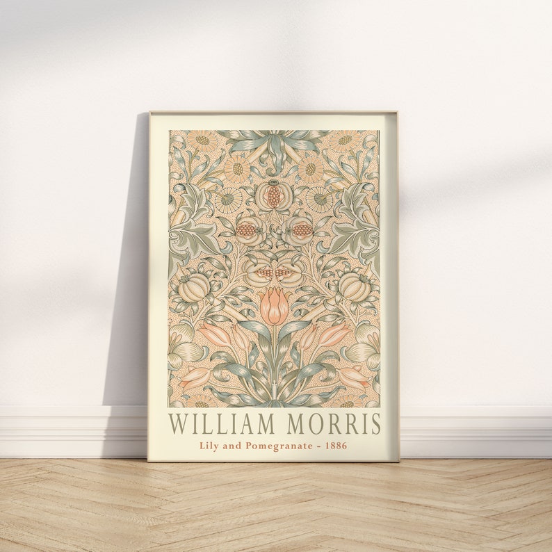 K&ouml;nnte beinhalten: Ein gerahmter Druck eines Vintage-Blumendesigns von William Morris mit dem Titel "Lily and Pomegranate - 1886". Das Design zeigt ein sich wiederholendes Muster aus Lilien, Granat&auml;pfeln und Bl&auml;ttern in Gr&uuml;n-, Rosa- und Cremet&ouml;nen.