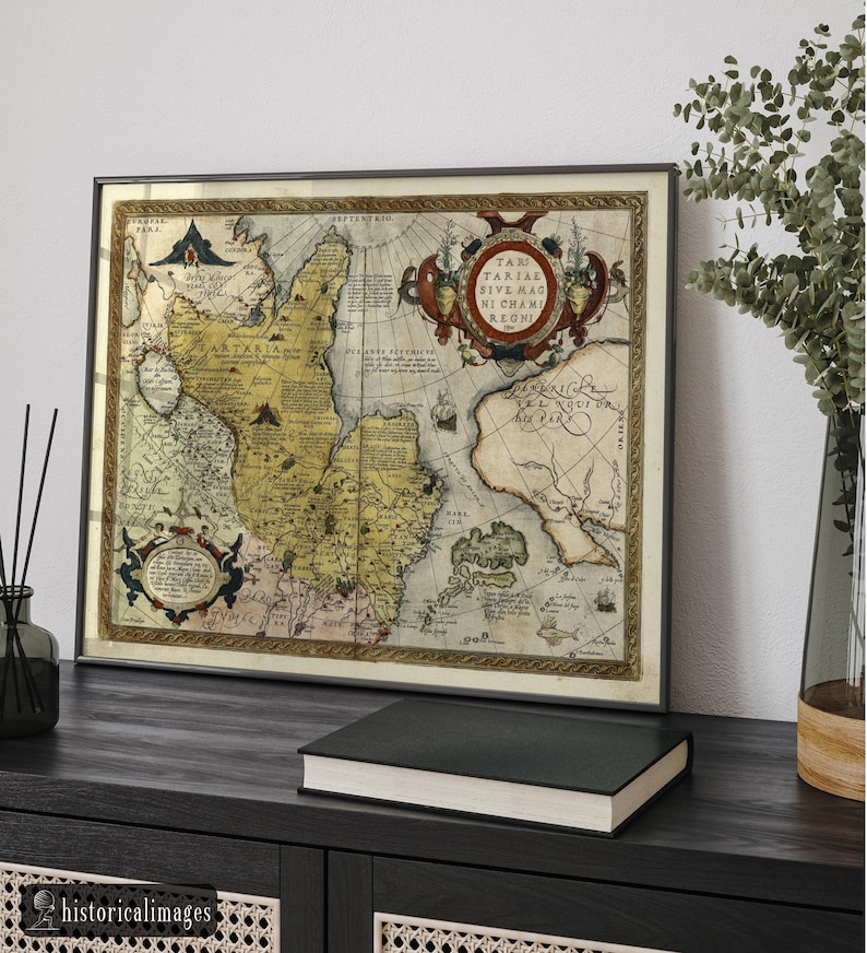 May include: Framed antique map with a detailed depiction of a historical region. The map features intricate cartography with various text elements and decorative borders. The frame is dark, and the map is displayed on a dark wooden surface with a book and a vase.