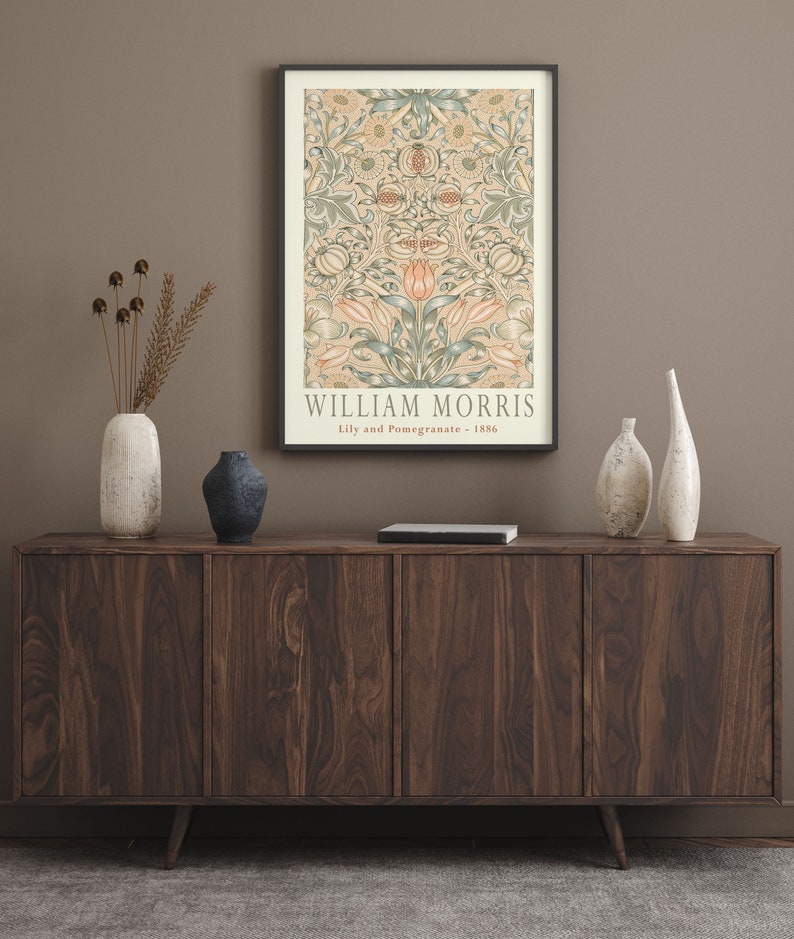 K&ouml;nnte beinhalten: Ein dunkles Holz Sideboard mit vier T&uuml;ren und einem schwarzen Buch darauf. Auf dem Sideboard stehen drei wei&szlig;e Keramikvasen und eine dunkelblaue Keramikvase. An der Wand hinter dem Sideboard h&auml;ngt ein gerahmtes Poster mit einem floralen Muster und dem Text "WILLIAM MORRIS Lily and Pomegranate - 1886".
