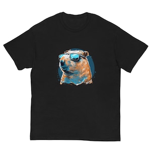 May include: Black t-shirt featuring a graphic of a capybara wearing sunglasses. The capybara is depicted in shades of orange, brown, and blue, set against a blue circular background. The t-shirt is made of a soft, comfortable material.