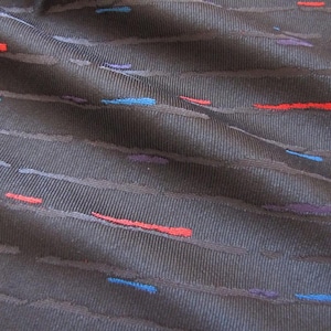 Puede incluir: Primer plano de una tela gris oscuro con textura acanalada. La tela presenta líneas horizontales con pequeños acentos coloridos en rojo, azul y morado. La tela tiene un brillo sutil.