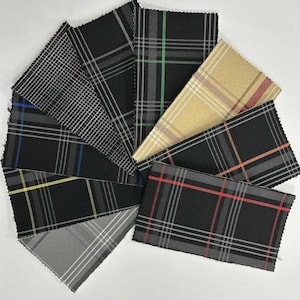 Op de afbeelding: Een verzameling stofstalen in verschillende ruitpatronen. De stalen tonen een reeks kleuren, waaronder zwart, grijs, beige en accenten van rood, groen en blauw. De stoffen zijn in een waaier gerangschikt, waarbij de verschillende ontwerpen worden getoond.