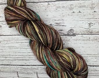 May include: A skein of yarn with brown, green, yellow, and turquoise stripes. The yarn is arranged in a loose coil.