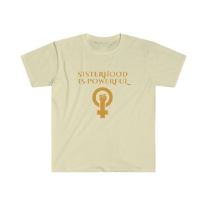 Puede incluir: Una camiseta beige claro con el texto "Sisterhood is Powerful" en letras doradas. Debajo del texto hay un símbolo femenino dorado con un puño en alto.