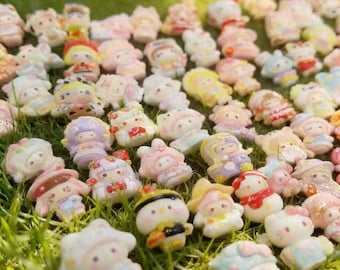 Puede incluir: Una colección de pequeñas figuras coloridas esparcidas sobre hierba verde. Las figuras presentan varios diseños, incluyendo personajes con sombreros, lazos y otros elementos decorativos. La paleta de colores incluye pasteles como el rosa, el amarillo y el azul.