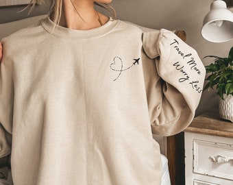 May include: A beige sweatshirt with a black airplane and heart design on the front and the text "Travel More Worry Less" on the sleeve.