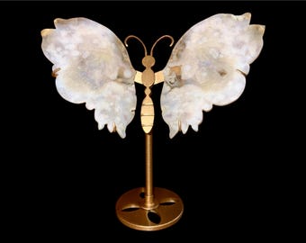 May include: A decorative butterfly sculpture with white and gray wings and a gold-colored metal frame and stand. The butterfly wings have a marbled appearance. The stand has a circular base.