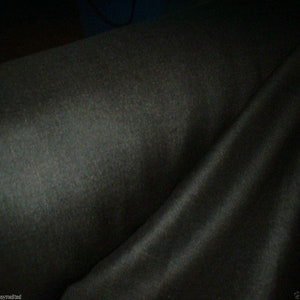 May include: A close-up of a dark grey fabric with a smooth, silky texture. The fabric is folded in half, creating a soft, flowing drape.