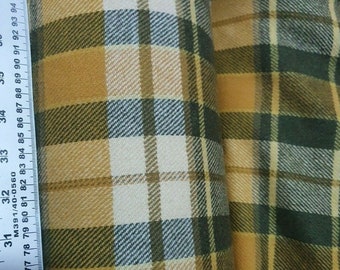 Op de afbeelding: Een close-up van een gele, groene en witte geruite stof. De stof wordt gemeten met een liniaal die inches en breuken van inches aangeeft.