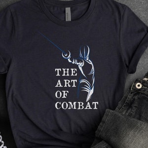 May include: Navy blue t-shirt with a fencing graphic and the text "THE ART OF COMBAT". The shirt is paired with black jeans, black high-top sneakers, and a brown belt. The word "NAVY" is at the bottom left.