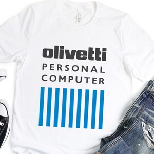 May include: White t-shirt with black text that reads "olivetti PERSONAL COMPUTER" and a blue and white striped design.