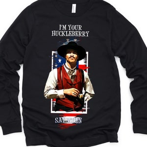 Puede incluir: Camiseta negra de manga larga con un gráfico de un hombre con un sombrero de vaquero y un chaleco. El texto "I'm your Huckleberry Say When" está impreso en la camiseta.