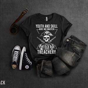 May include: Black t-shirt with a white skull and crossbones graphic. The text reads "Youth and skill are no match for old age and treachery".