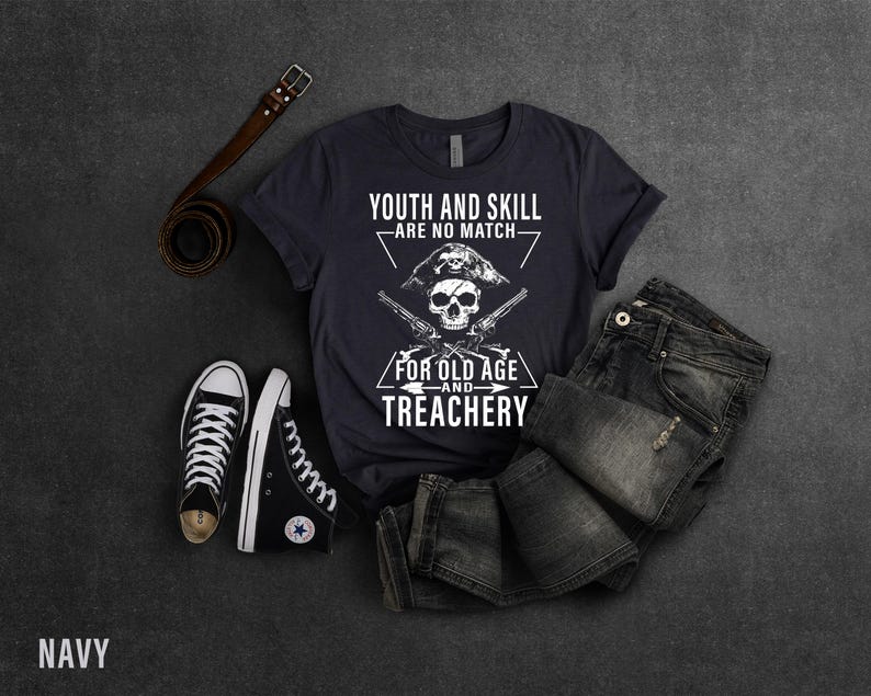 May include: A navy blue t-shirt with a white skull and crossbones graphic. The text on the shirt reads "Youth and Skill - Are No Match - For Old Age and Treachery".