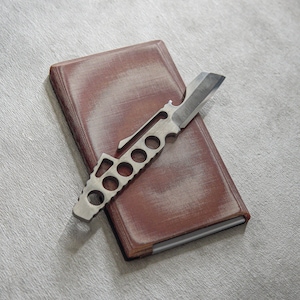 May include: A brown leather bound journal with a silver multi-tool knife on top.