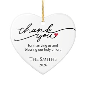 May include: A white heart-shaped ceramic ornament with a gold hanging string. It features black cursive text that reads thank you with a small red heart, followed by the text for marrying us and blessing our holy union, The Smiths, and 2026.