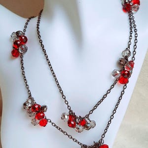 May include: A layered necklace with two chains and red and clear glass beads. The beads are clustered together in groups, creating a cascading effect.