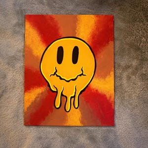 Op de afbeelding: Vierkant canvas schilderij met een gele, smeltende smiley tegen een achtergrond van stralende oranje, rode en bruine tinten. Het kunstwerk heeft een retro, psychedelische uitstraling.