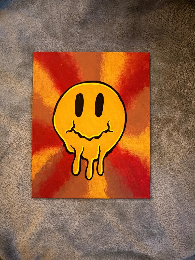Op de afbeelding: Vierkant canvas schilderij met een gele, smeltende smiley tegen een achtergrond van stralende oranje, rode en bruine tinten. Het kunstwerk heeft een retro, psychedelische uitstraling.