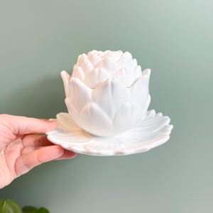 May include: A white ceramic mug with a black handle and the text "But First, Coffee" in a black, handwritten-style font. The mug is on a white surface.