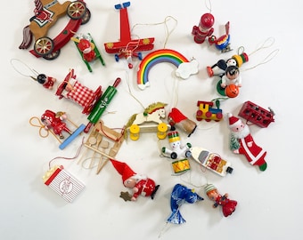 May include: A collection of vintage Christmas ornaments in various shapes and colors. Includes a rocking horse, airplane, rainbow, Santa Claus, train, and popcorn box. Ornaments are made of wood and painted with bright colors.